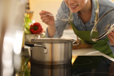 Woman tasting fresh bouillon in kitchen, closeup. Homemade recipe