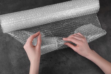Woman covering wineglass with bubble wrap at dark grey table, closeup