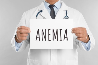 Doctor holding sign with word ANEMIA on light grey background, closeup