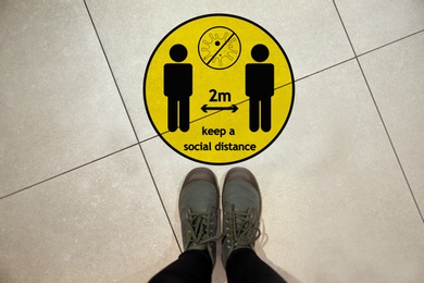 Image of Keep social distance as preventive measure during coronavirus outbreak. Yellow warning sign on floor in front of woman, closeup