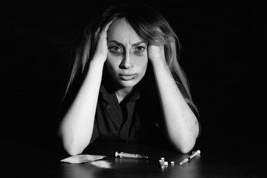 Addicted woman at table with different drugs, black and white effect