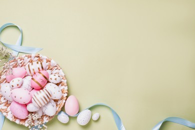 Photo of Flat lay composition with festively decorated Easter eggs and ribbon on pale olive color background. Space for text