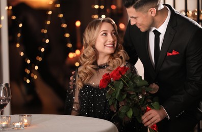 Man presenting roses to his beloved woman in restaurant at Valentine's day dinner