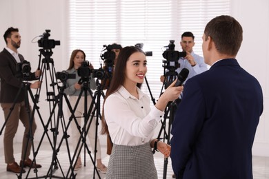 Professional young journalist interviewing businessman and group of video camera operators on background