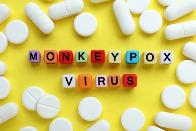 Photo of Words Monkeypox Virus made of colorful plastic beads and pills on yellow background, flat lay