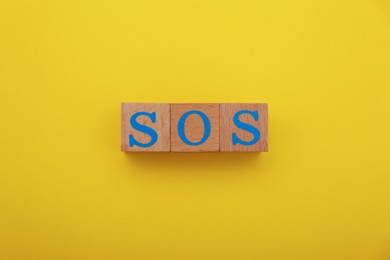 Abbreviation SOS made of wooden cubes on yellow background, top view