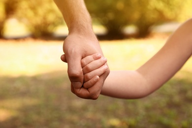 Little child and father holding hands outdoors, closeup. Family weekend
