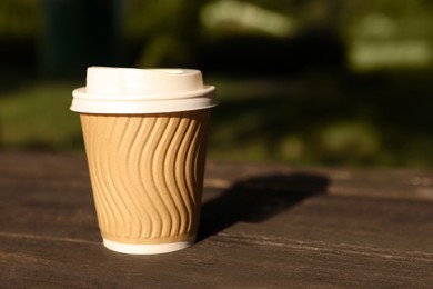Paper cup on wooden table outdoors, closeup with space for text. Coffee to go