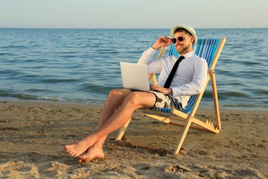 Photo of Happy man with laptop on deckchair near sea. Business trip