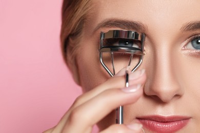Young woman with eyelash curler on pink background, closeup