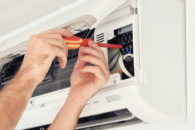Electrician with screwdriver fixing air conditioner indoors, closeup