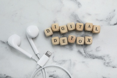 Cubes with phrase DIGITAL DETOX and earphones on white marble table, flat lay