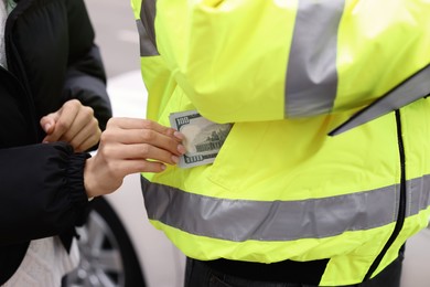 Woman putting bribe into police officer's pocket, closeup