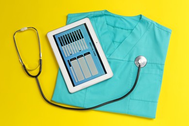 Photo of Medical uniform, tablet and stethoscope on yellow background, flat lay
