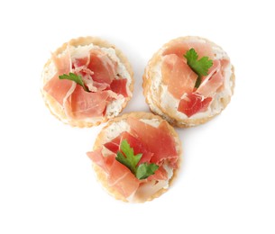 Delicious crackers with cream cheese, prosciutto and parsley on white background, top view