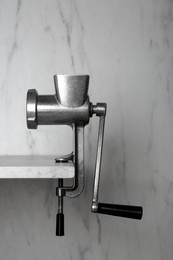 Photo of Metal manual meat grinder on table against white marble background
