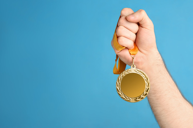 Man holding silver medal on blue background, closeup. Space for design