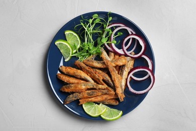 Photo of Plate with delicious fried anchovies, lime slices, microgreens and onion rings on light table, top view