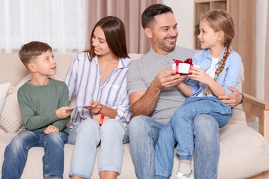 Photo of Cute little children presenting their parents with gifts on sofa at home