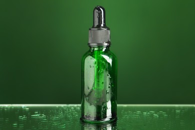 Bottle of face serum on wet surface against green background, closeup