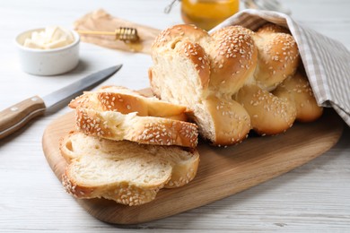 Cut freshly baked braided bread, knife and butter on white wooden table, closeup. Traditional Shabbat challah