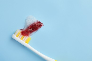 Photo of Toothbrush with blood on light blue background, top view and space for text. Gum inflammation