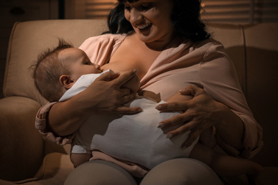 Photo of Woman breastfeeding her little baby on sofa in evening