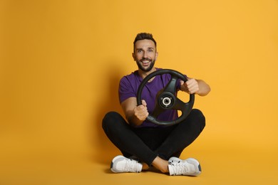 Happy man with steering wheel on yellow background