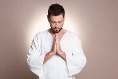 Religious man with clasped hands praying against grey background