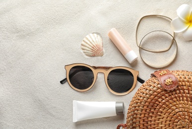 Flat lay composition with sun protection cosmetic products on sand, space for text