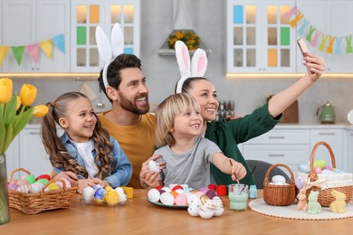 Photo of Family making selfie while painting Easter eggs at table in kitchen