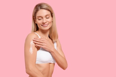 Photo of Woman applying body cream onto her arm against pink background, space for text