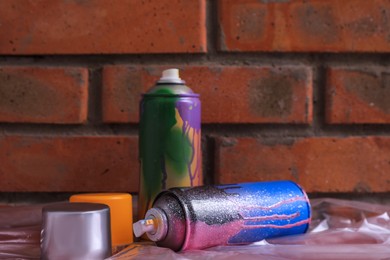 Used cans of spray paints on table near brick wall. Graffiti supplies