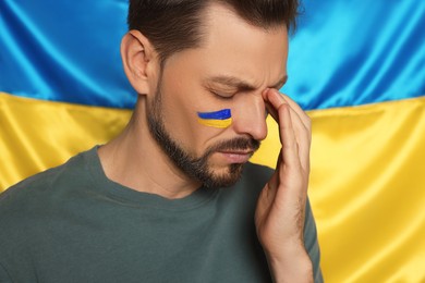 Photo of Sad man with face paint near Ukrainian flag, closeup