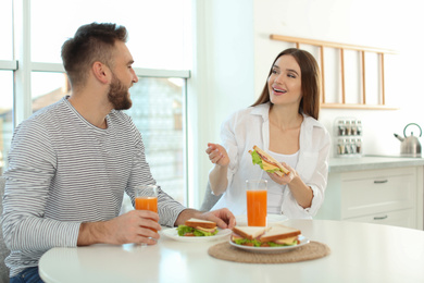 Photo of Happy couple having breakfast with sandwiches at table in kitchen