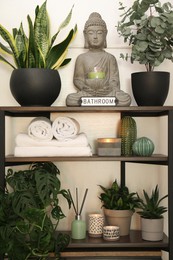 Photo of Shelving unit with stylish decor, towels and green houseplants in bathroom. Interior design