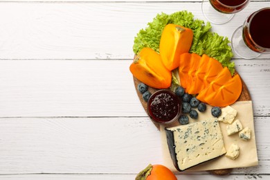 Photo of Delicious persimmon, blue cheese, blueberries and jam served on white wooden table, flat lay. Space for text