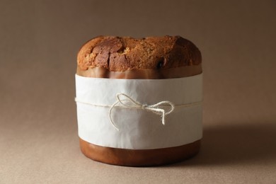Photo of Delicious Panettone cake wrapped in parchment paper on light brown background. Traditional Italian pastry