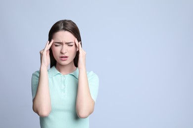 Young woman suffering from headache on light background, space for text