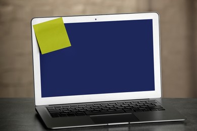 Laptop with blank sticky note on grey office desk. Space for text