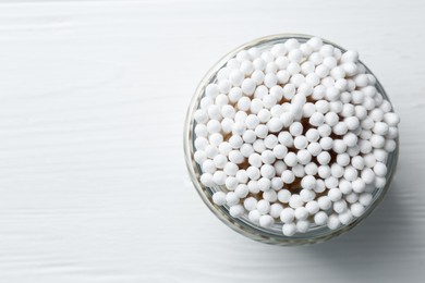 Many cotton buds in glass jar on white wooden table, top view. Space for text