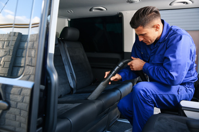 Car wash worker vacuuming upholstery on automobile seat