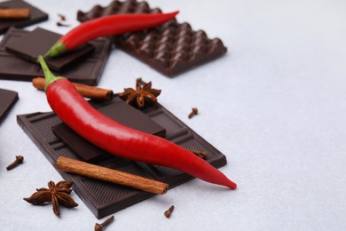 Photo of Delicious chocolate, fresh red chili peppers and spices on white table, closeup. Space for text