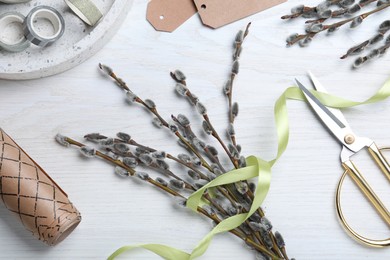 Beautiful bouquet of pussy willow branches and wrapping materials on white wooden table, flat lay