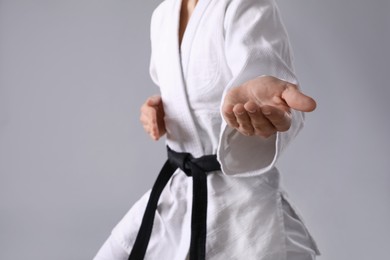 Martial arts master in keikogi with black belt against grey background, focus on hand
