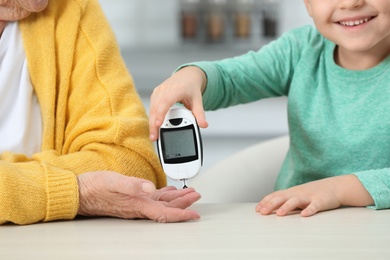 Senior woman with her grandson using digital glucometer at home, closeup. Diabetes control
