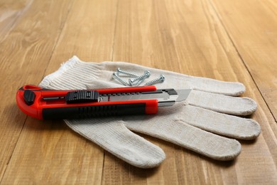 Photo of Utility knife, screws and glove on wooden table