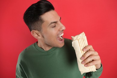 Man eating delicious shawarma on red background