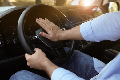Photo of Man pressing horn in car, closeup. Aggressive driving behavior