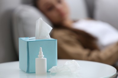 Photo of Ill woman at home, focus on nasal spray and box of tissues